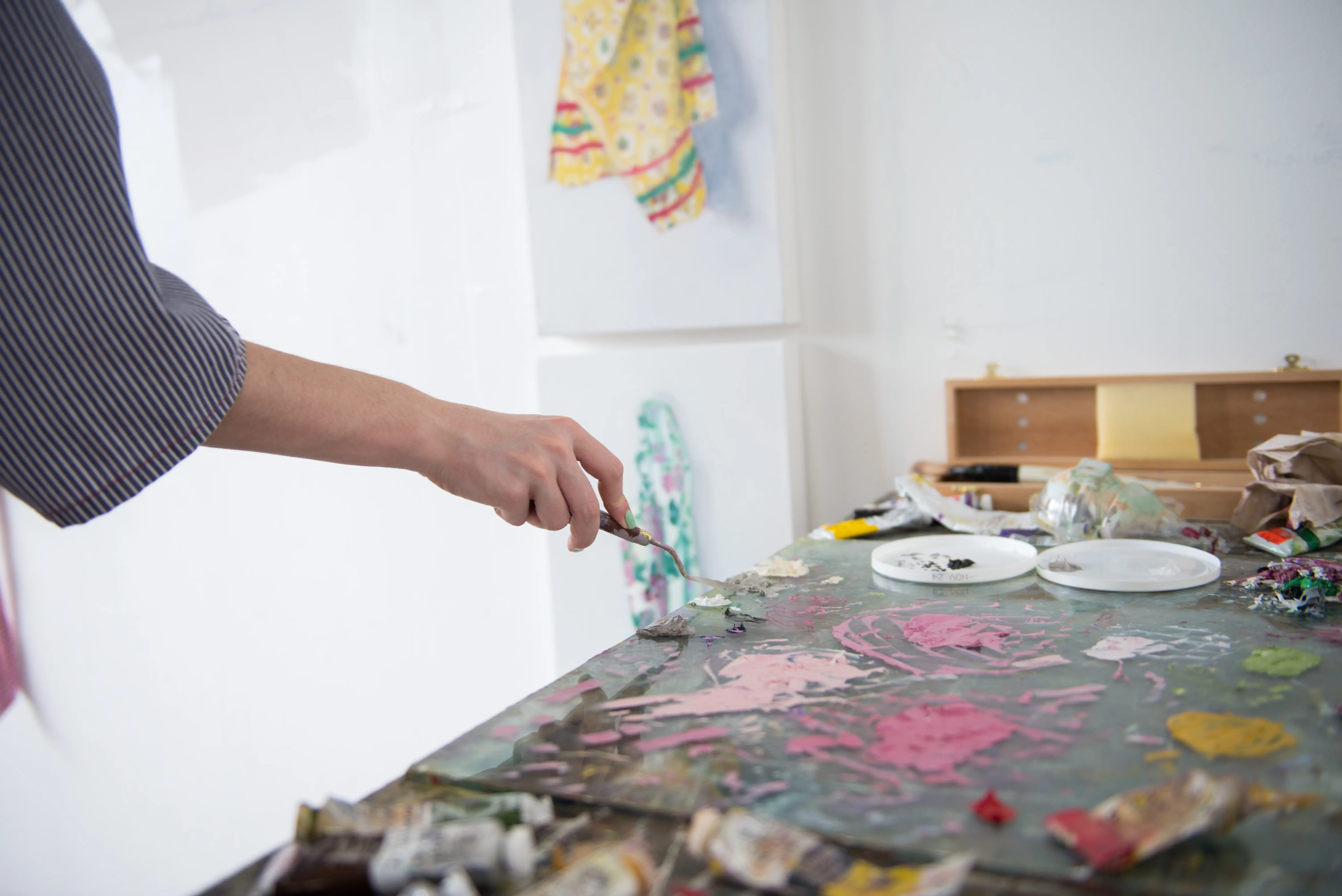 Person using a palette knife on a tabletop covered in colorful paint.